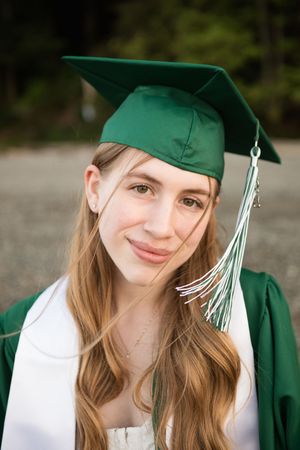 A graduate wearing an emerald green cap and gown smiles warmly during their graduation photo session.