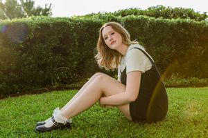 Person lying in green grass wearing white top and denim shorts on a sunny summer day.
