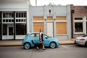 A panoramic street view showing boarded-up buildings and a light blue vintage car parked along an urban sidewalk.