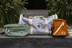 Various Kånken crossbody bags and backpacks in different colors and styles displayed in an outdoor setting.