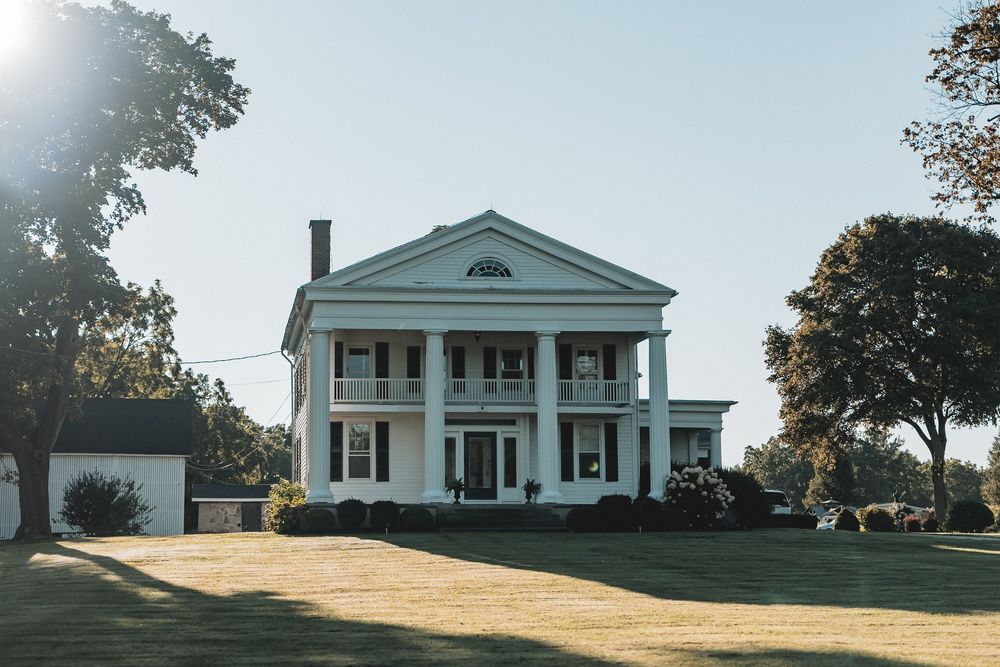 Stately white antebellum mansion with tall columns and Greek Revival architecture stands on a sunny lawn.