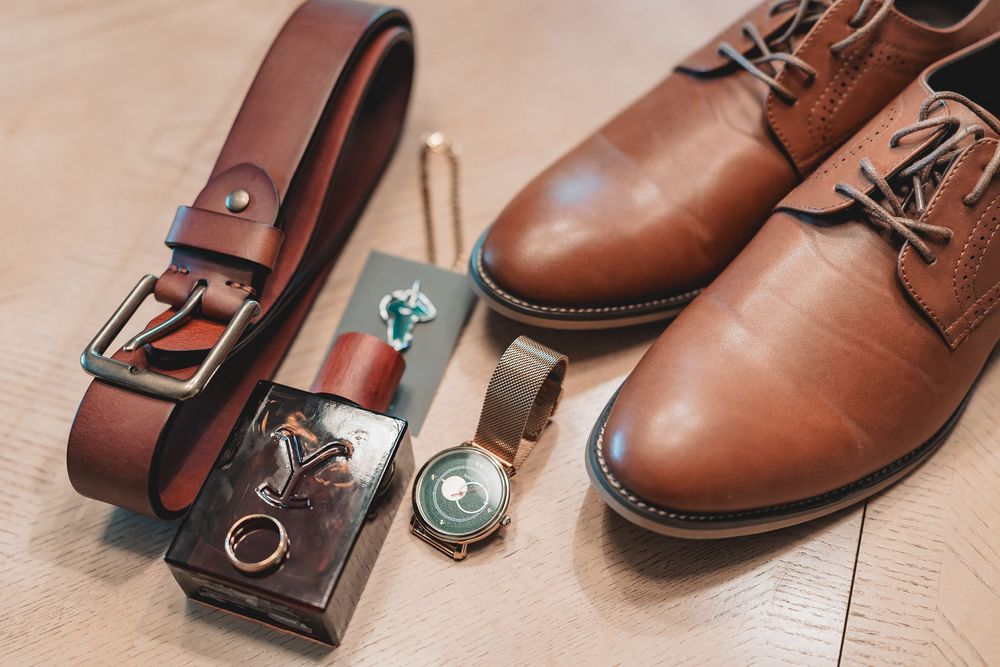 Close-up view of brown leather dress shoes and matching belts arranged on light wooden flooring.