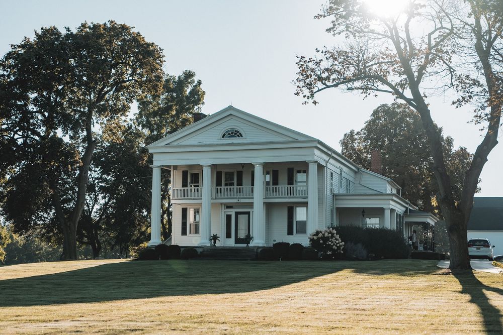 A panoramic view of a white southern-style plantation home with columned porches set on a rolling green lawn.
