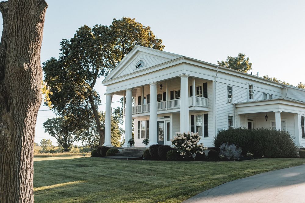 White colonial style house with pillars and portico viewed from multiple angles on a grassy hillside property.