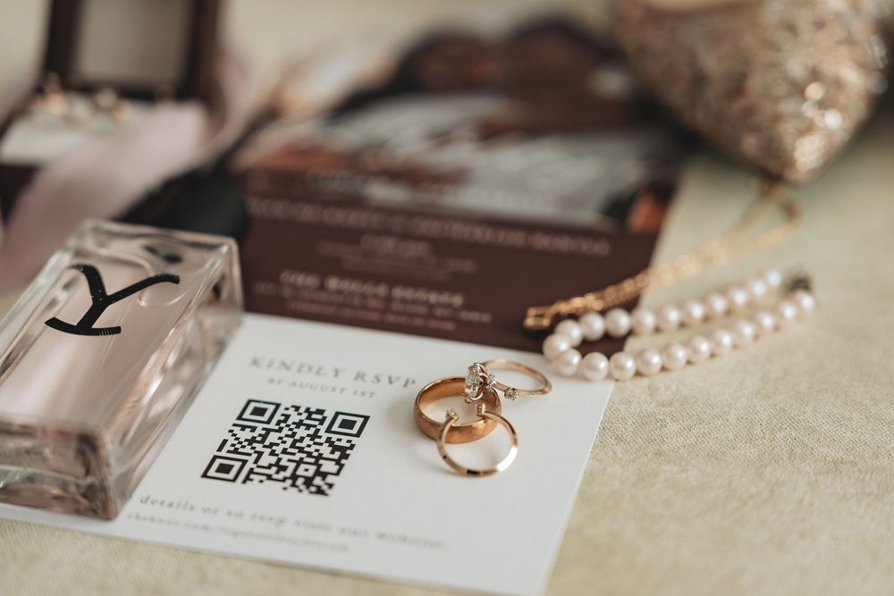 Wedding details including rings, pearl necklace, and invitation cards arranged on a textured beige surface.