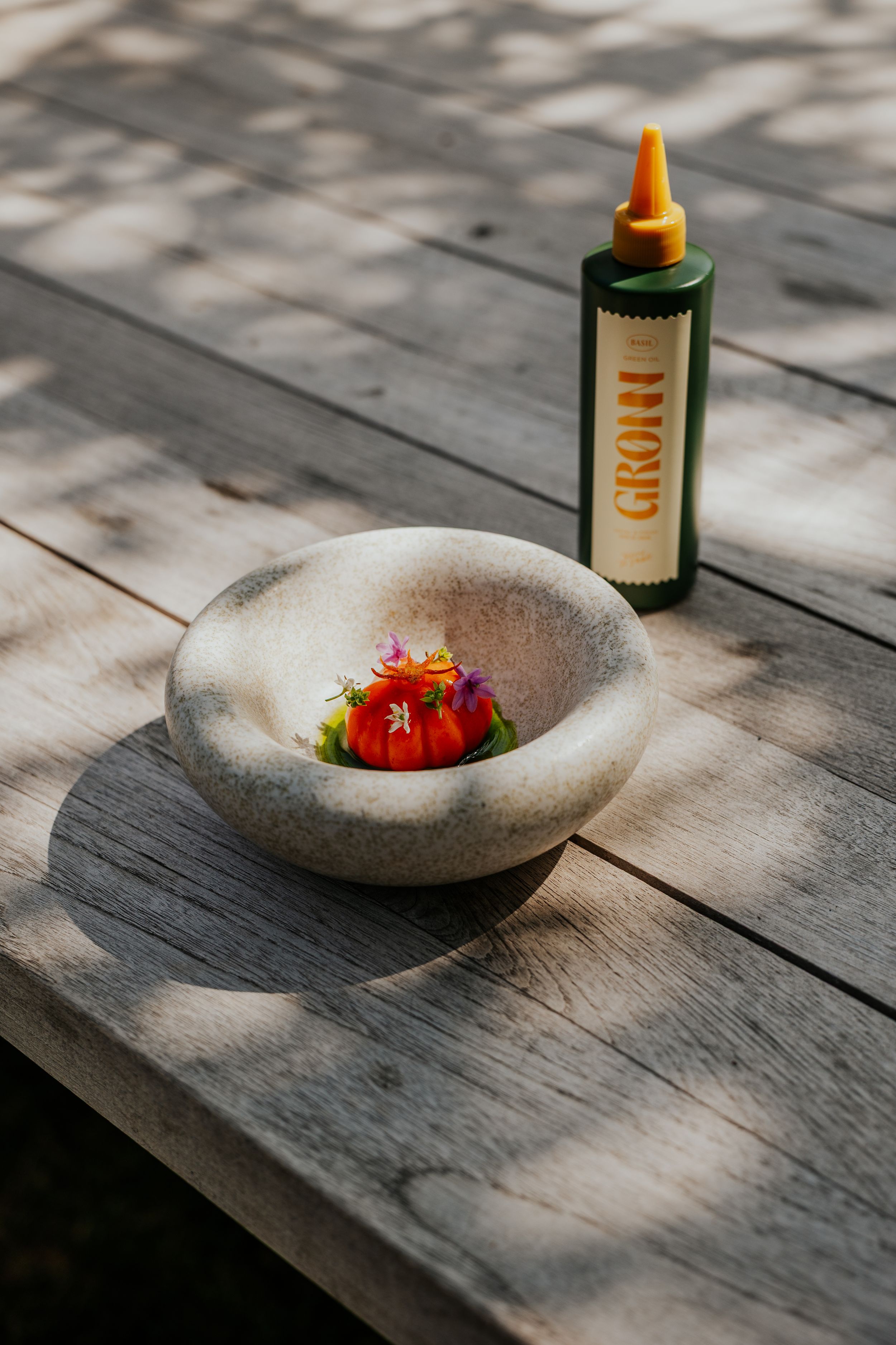 Artfully plated dish with strawberries in a stone bowl on a weathered wooden surface.