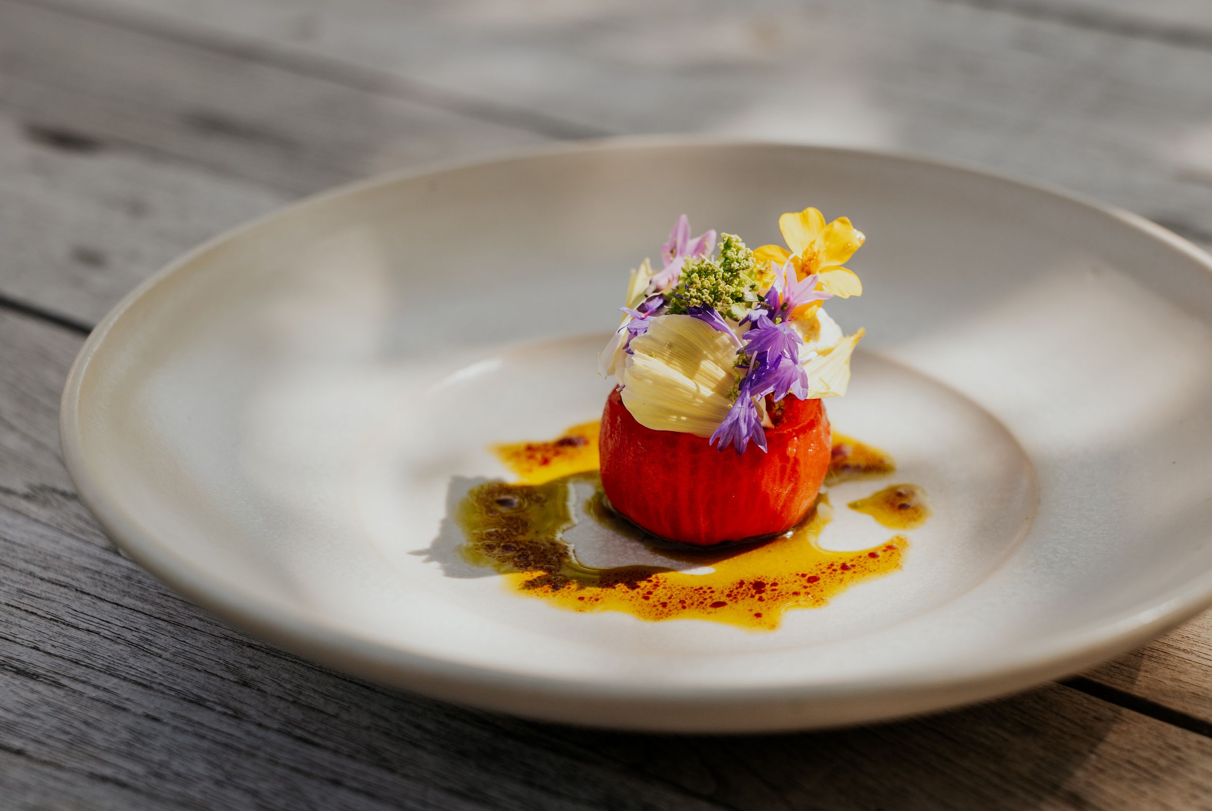 Beautifully plated dish with colorful edible flowers and sauce on white ceramic plate.
