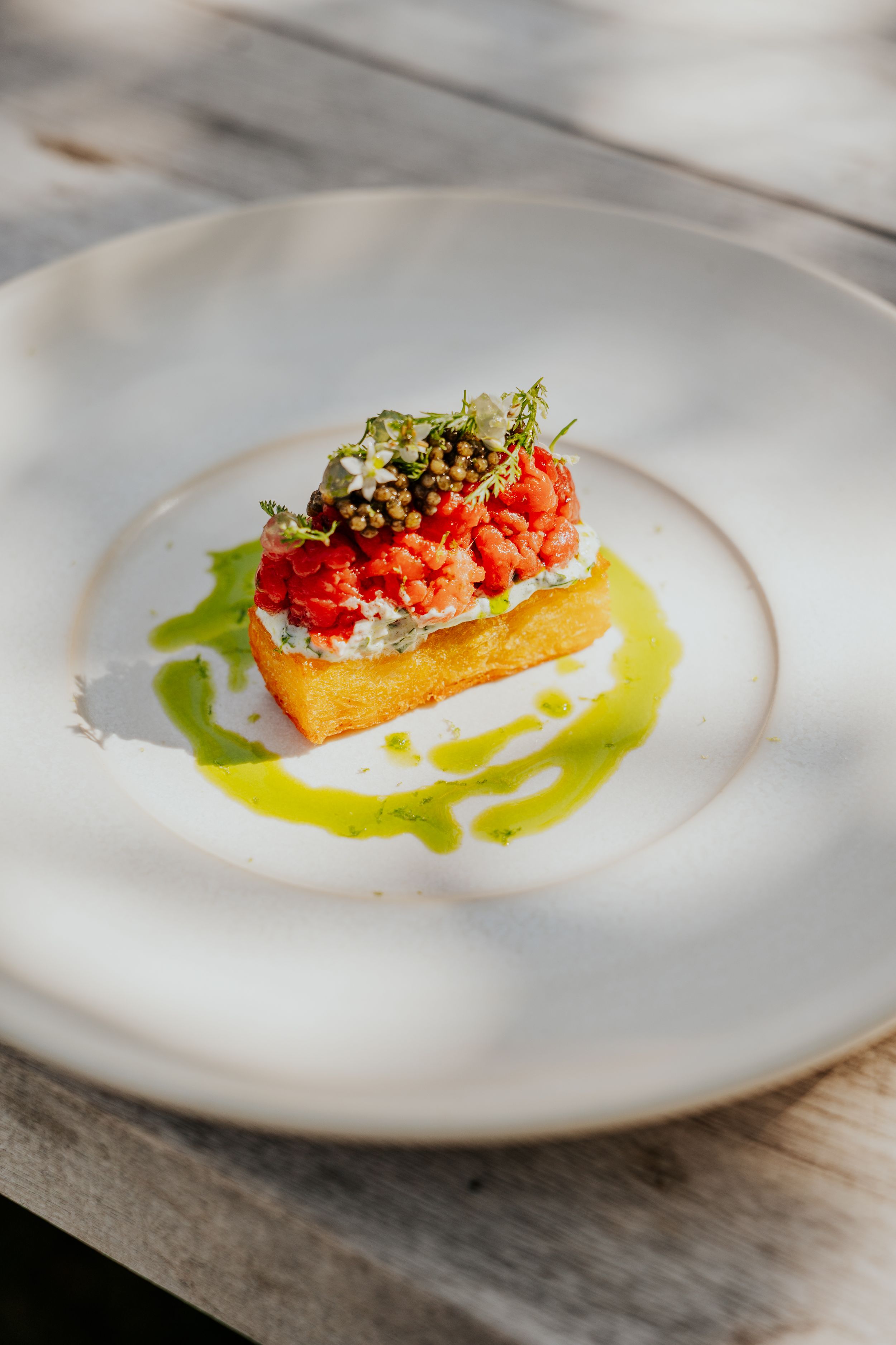 Modern fine dining dish with vibrant orange components and green sauce on white plate.