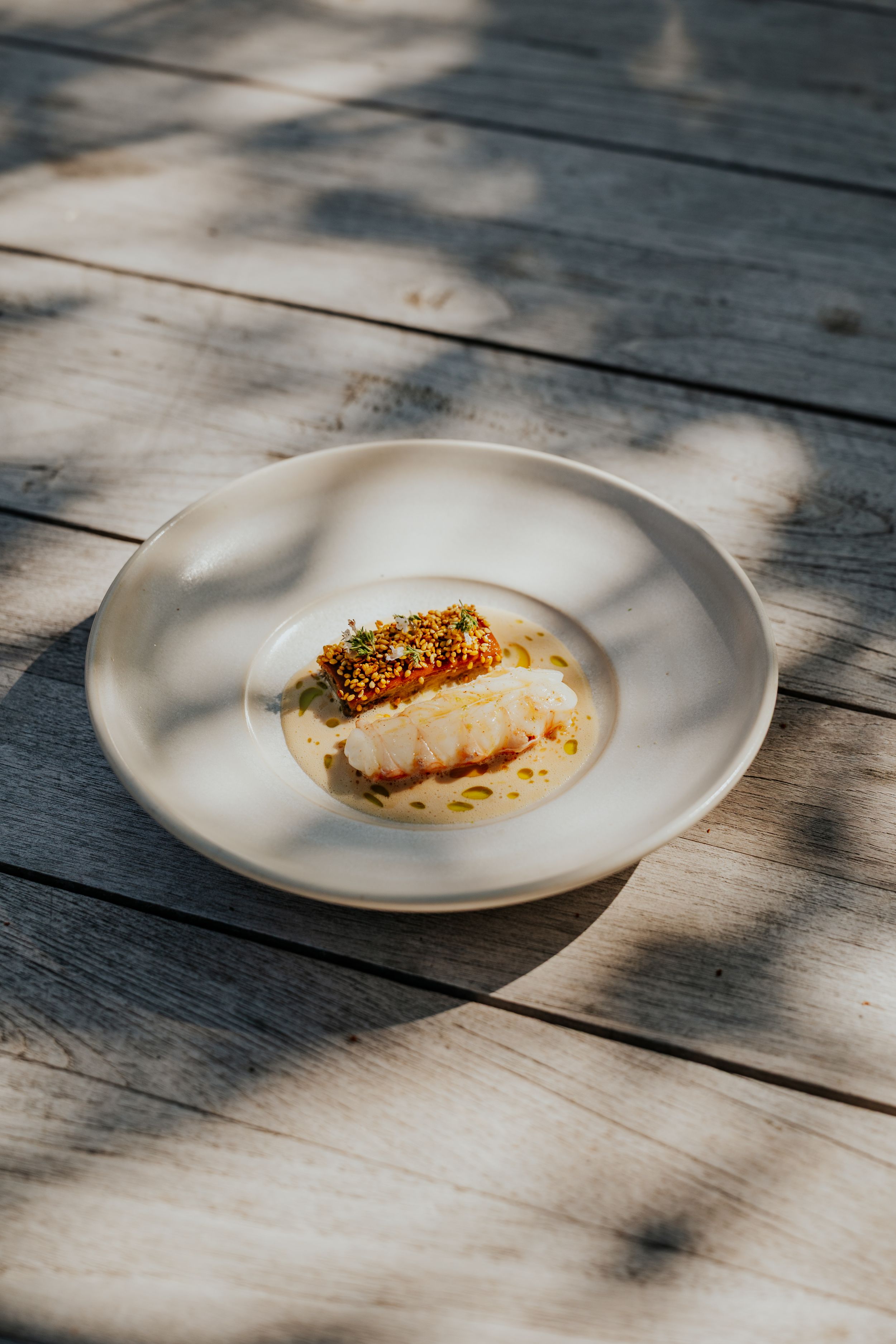 Minimalist plated seafood dish with garnish on white ceramic plate against wooden surface.