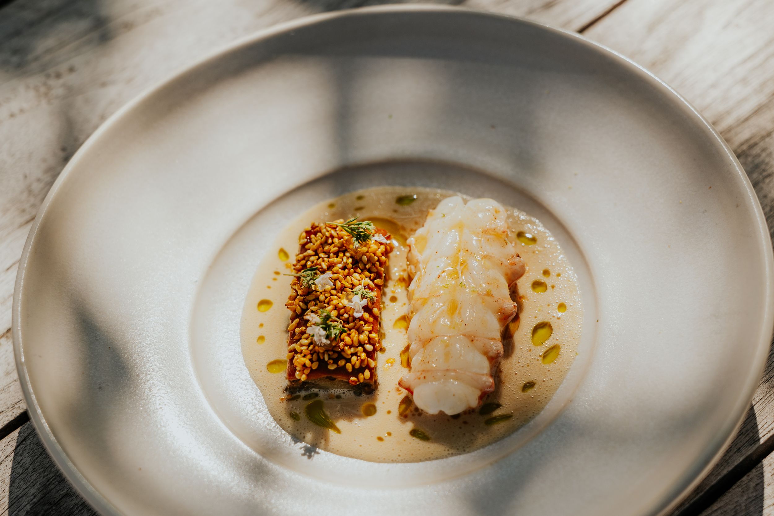 Elegant plated fish dish with golden crispy topping on white ceramic plate.