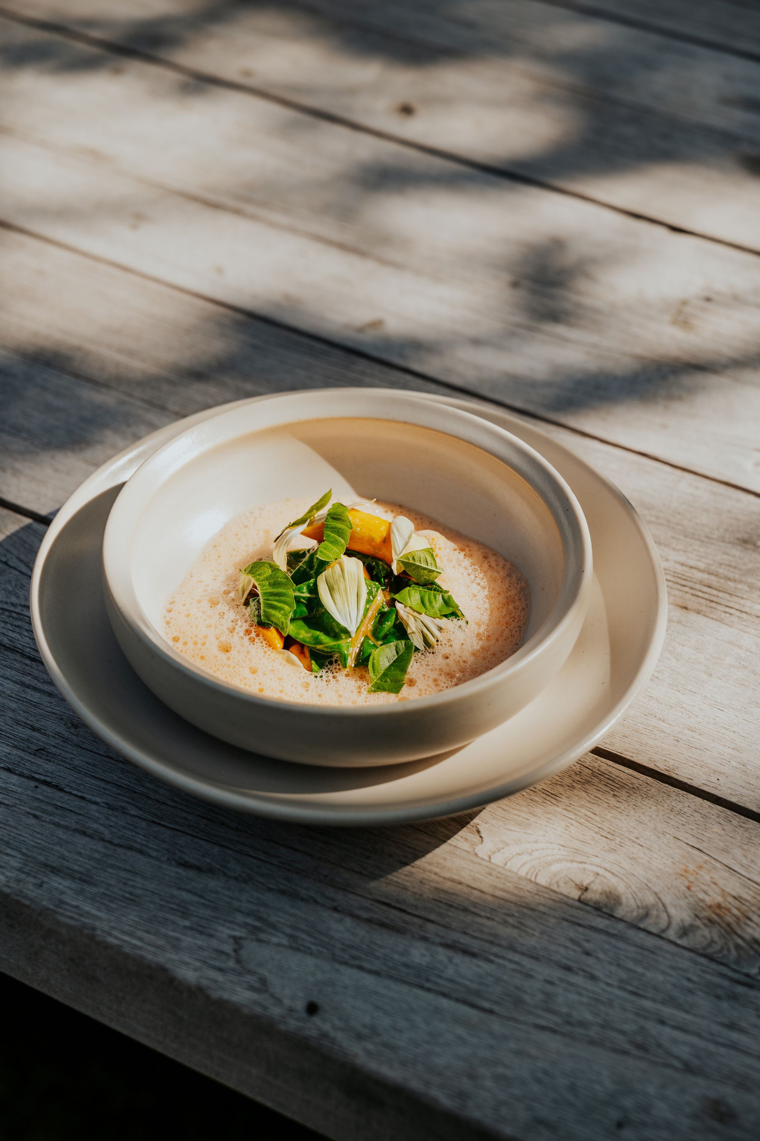 Gourmet soup dish with fresh green garnishes served on white plate with natural lighting.