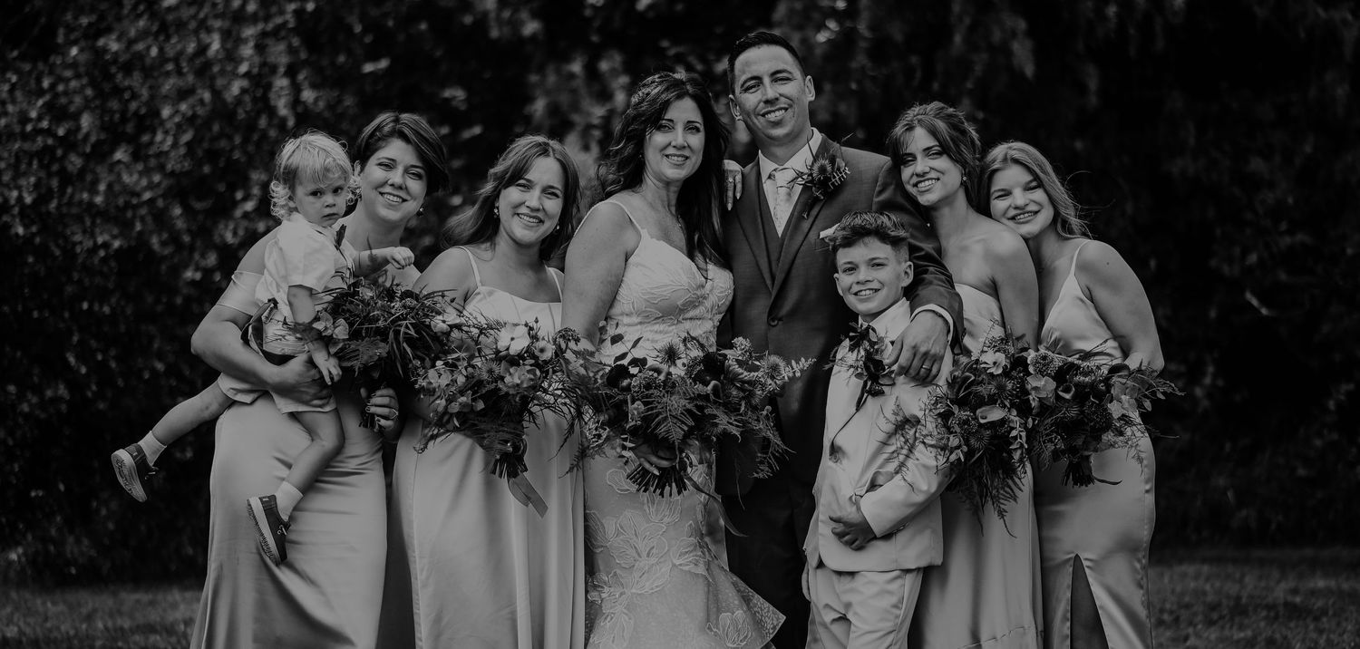 Black and white wedding party portrait showing bridal group with matching gowns and bouquets posing outdoors.