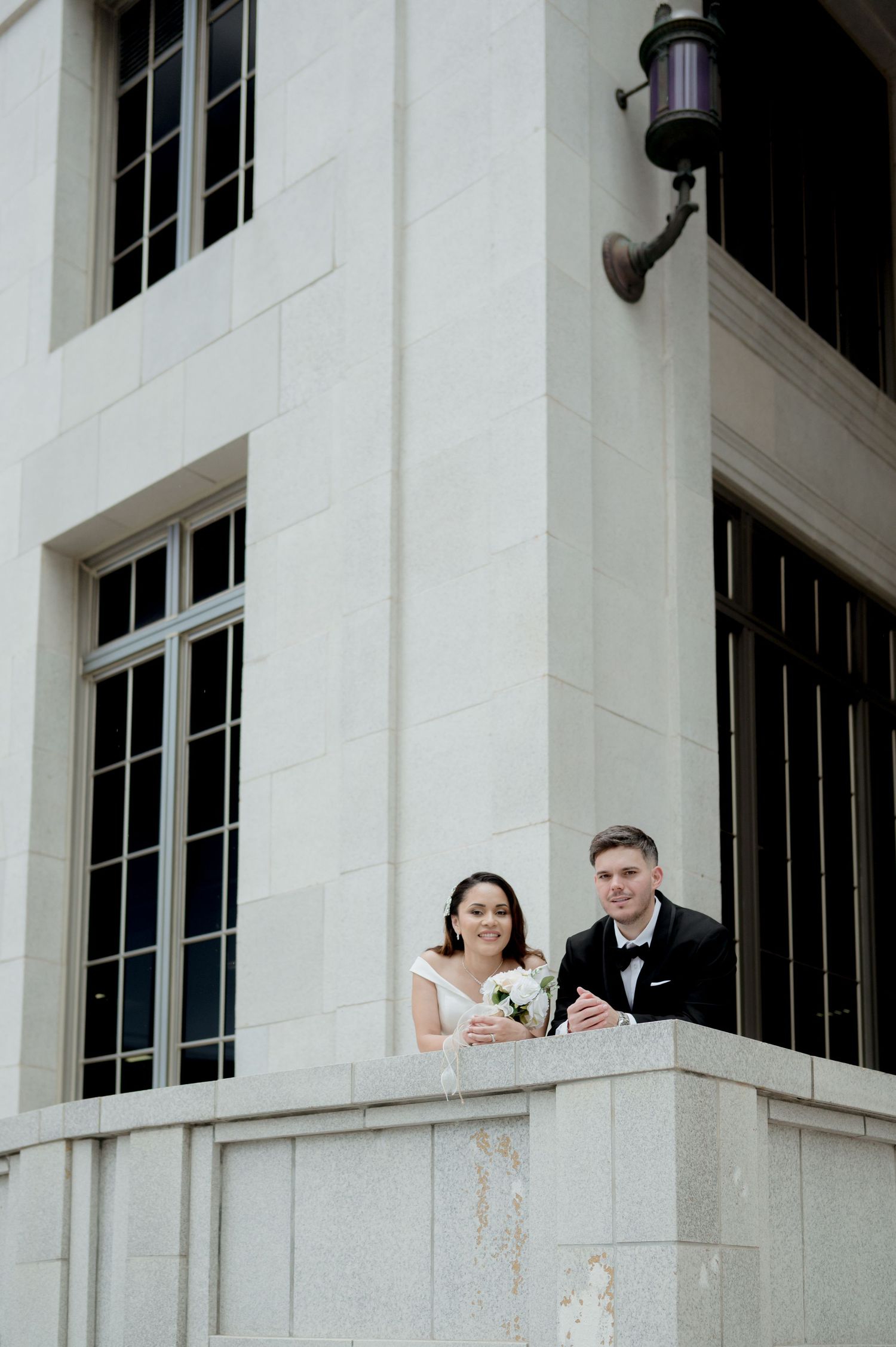 Wedding party members peek out from behind white pillars of an elegant building in playful poses during formal portraits.