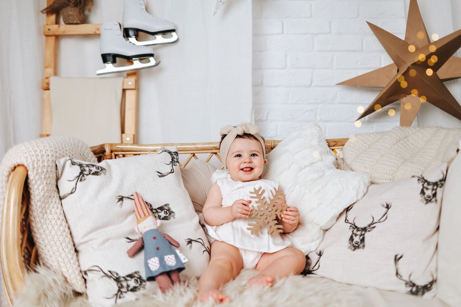 Baby sitting on couch with holiday decorations and ice skates hanging on wall.