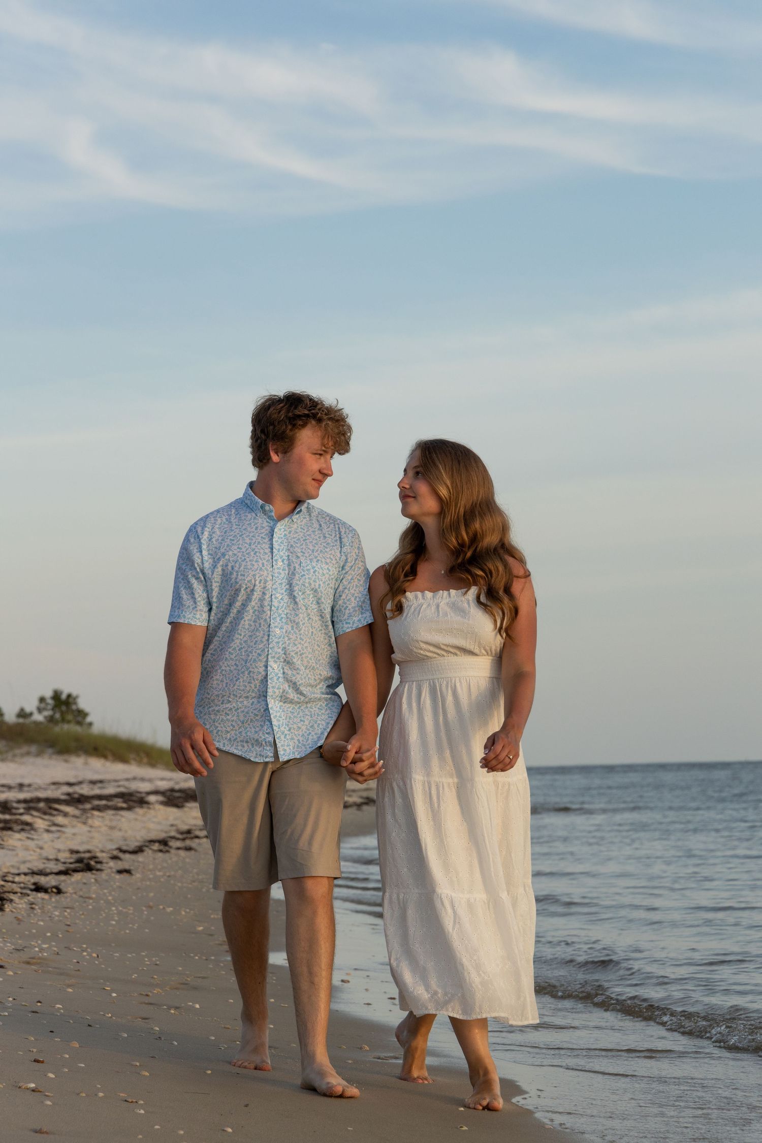 Romantic couple walking hand in hand along beach shoreline at sunset.