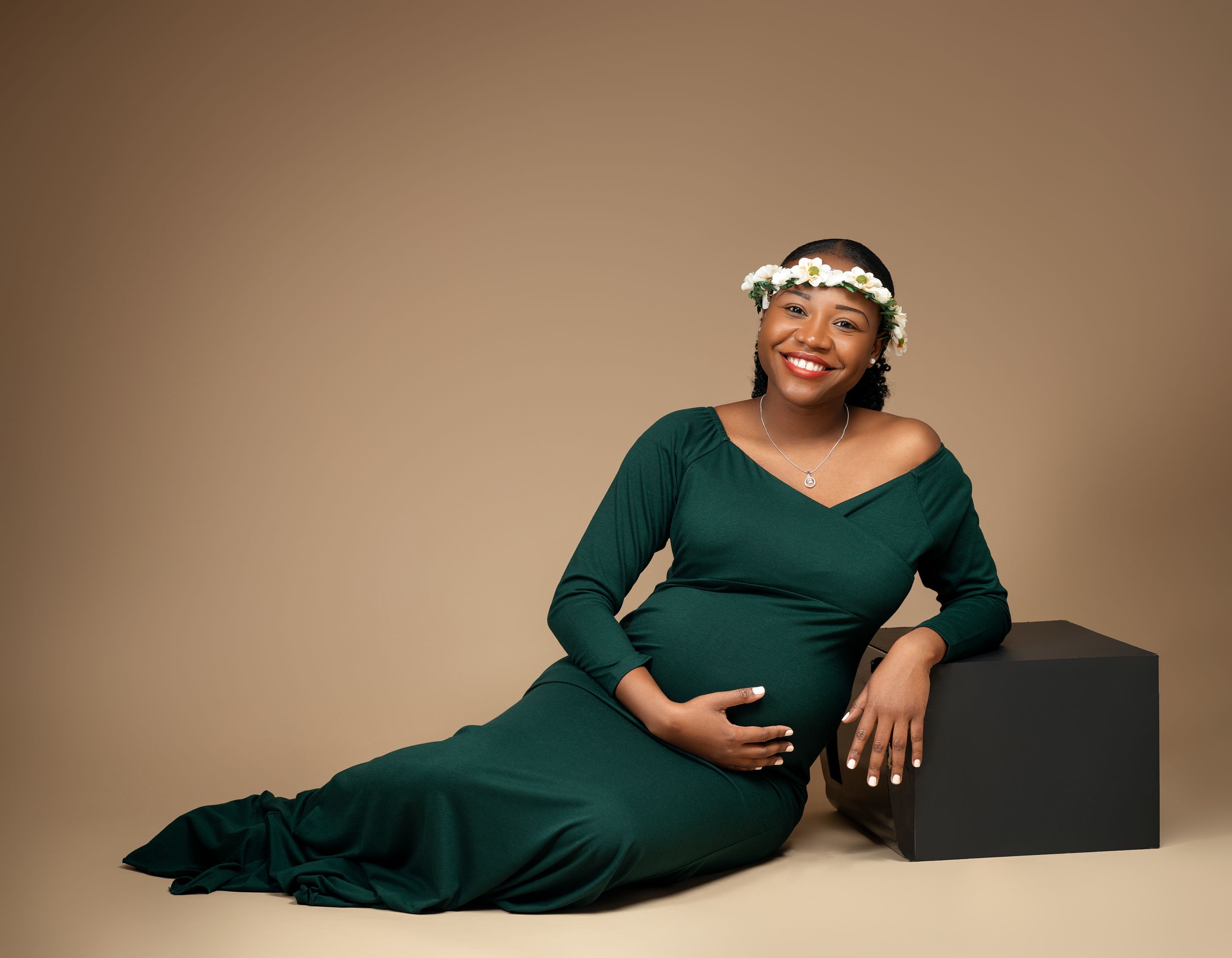Maternity portrait featuring person in emerald green dress reclining against dark geometric prop.