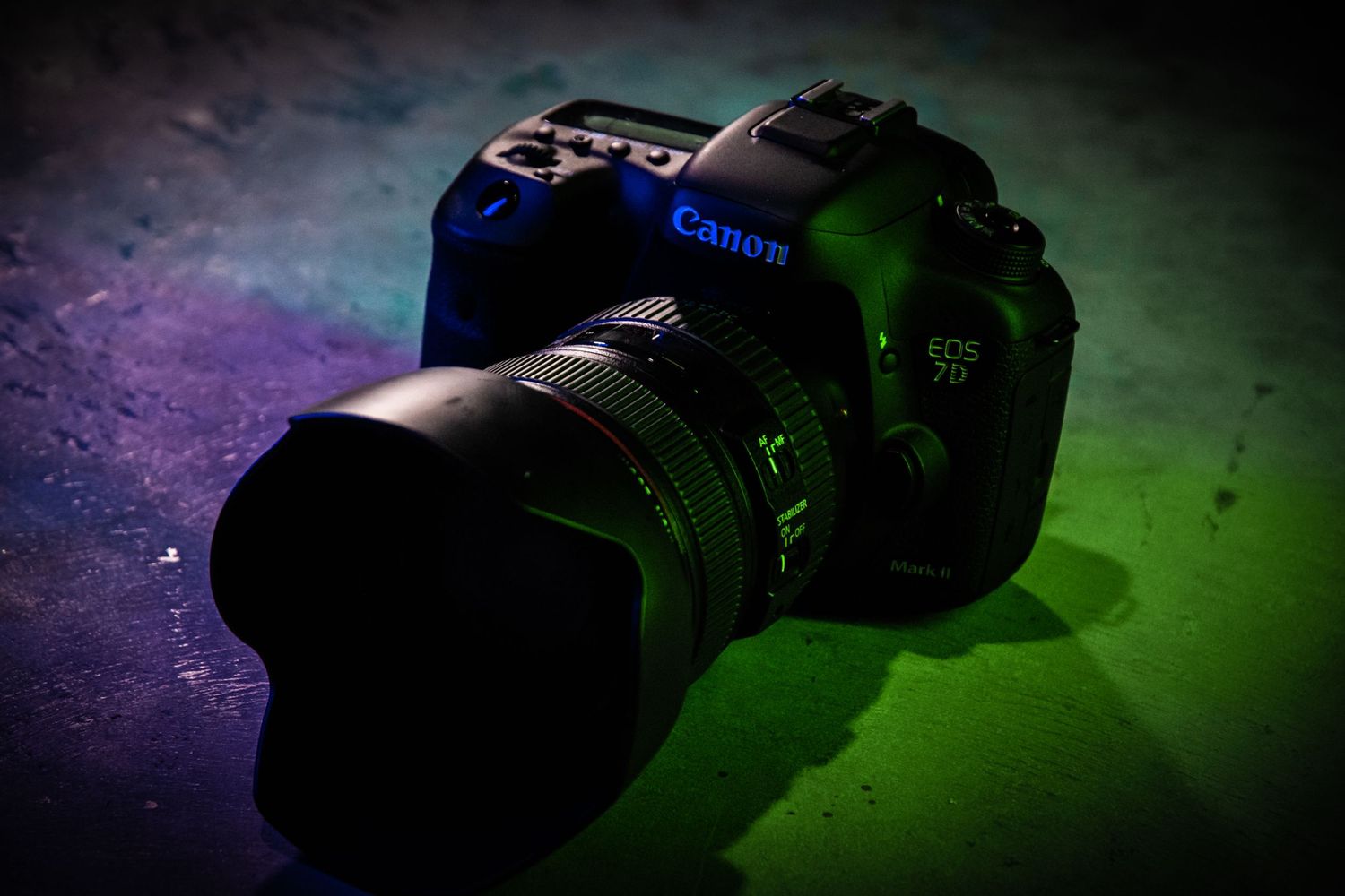 Canon DSLR camera with telephoto lens on dark surface with colorful lighting effects.
