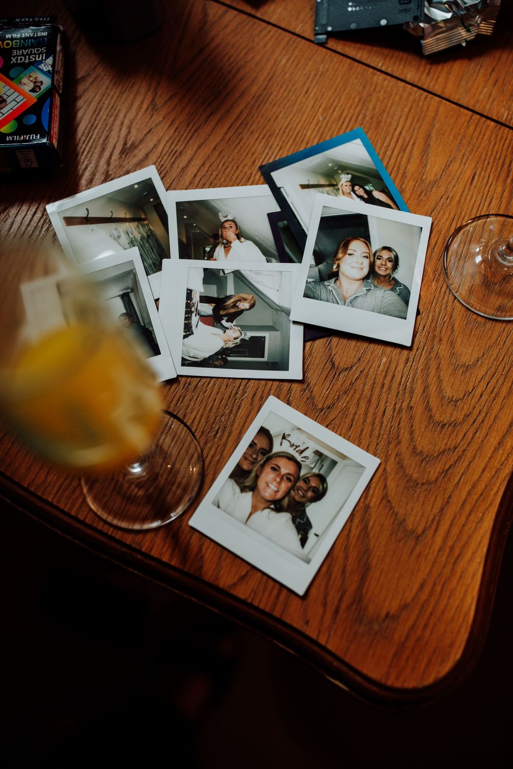 Polaroid photos scattered on wooden table next to orange cocktail.