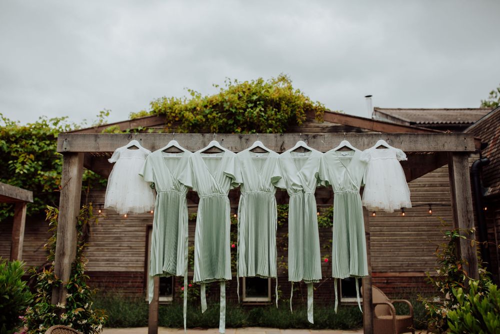 Row of mint green bridesmaid dresses hanging on wooden wall outdoors.