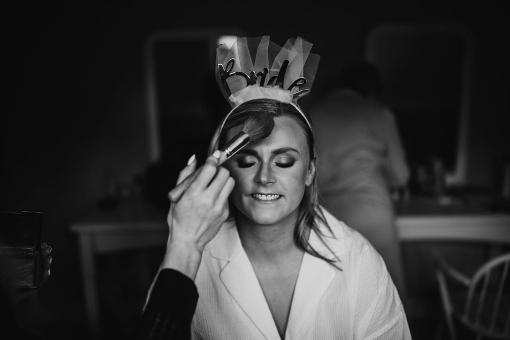 Black and white image showing wedding makeup application in progress.