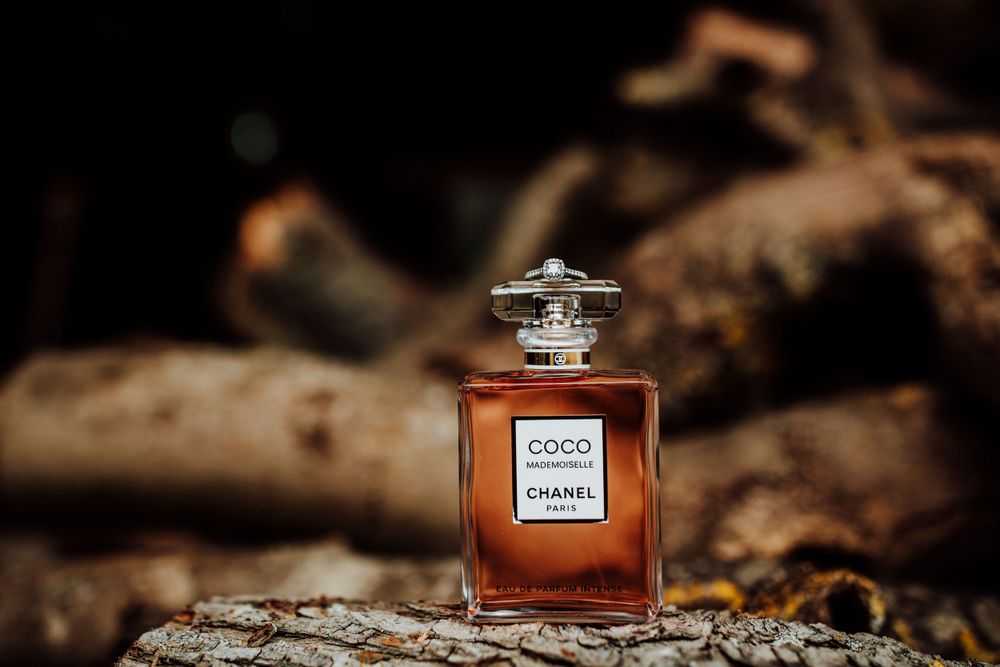 Chanel Coco perfume bottle positioned on rustic wooden surface with moody lighting.