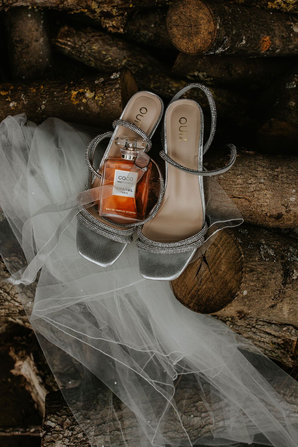 Elegant silver wedding shoes and perfume bottle arranged with tulle on wooden surface.