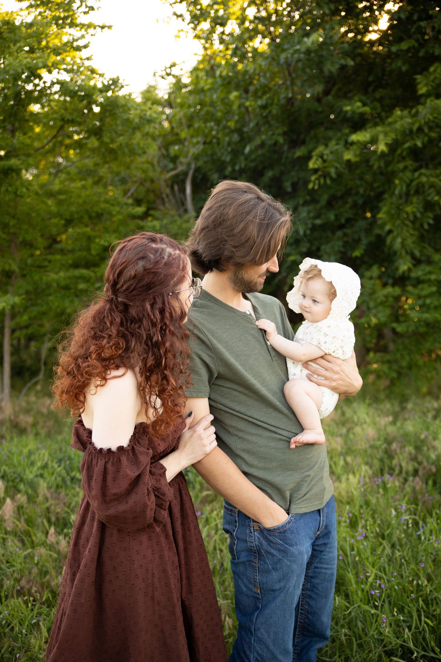 A family stands together in a natural outdoor setting with green foliage during golden hour.