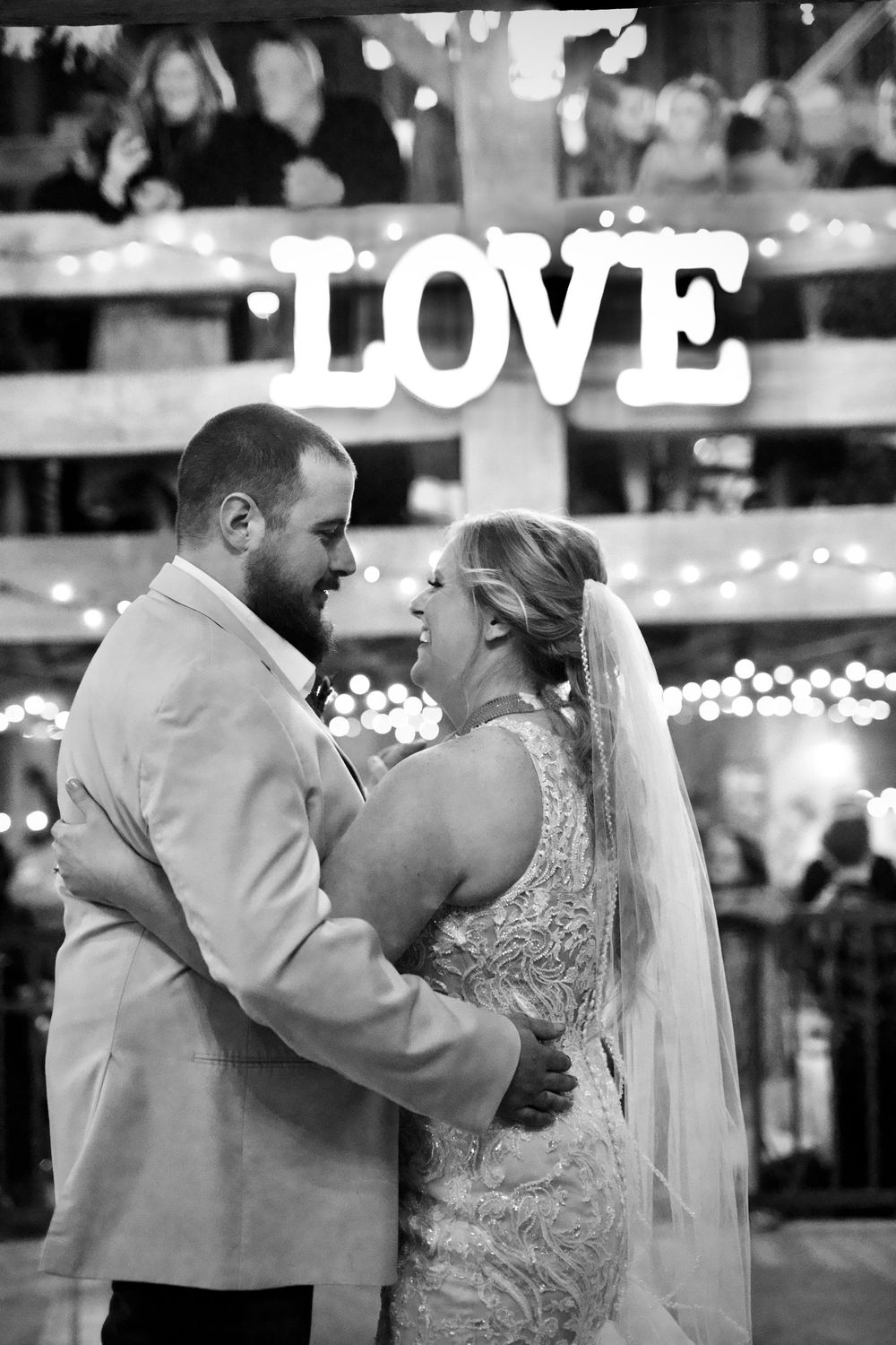 Romantic first dance between newlyweds under twinkling lights with 'LOVE' sign visible in background.