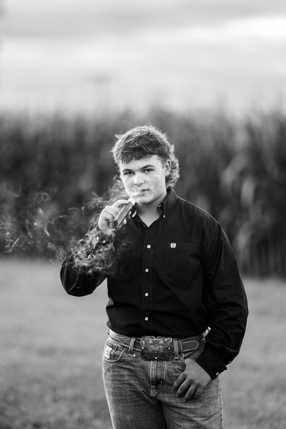 Black and white portrait of someone in a dark shirt smoking against a blurred outdoor background.