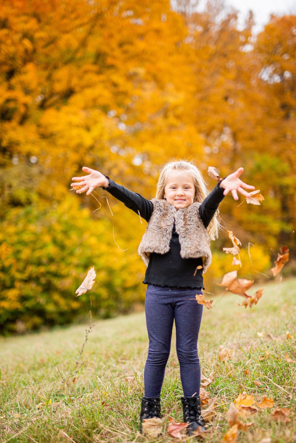 Child playing with autumn leaves against vibrant orange fall foliage background.