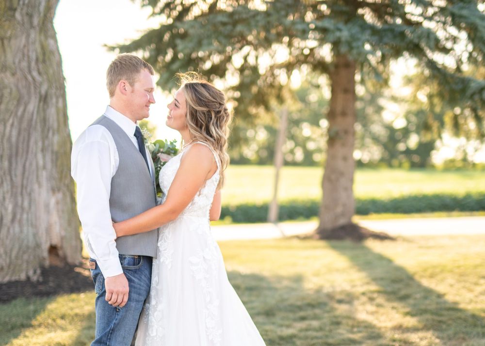 Newlywed couple shares intimate moment outdoors under large trees.