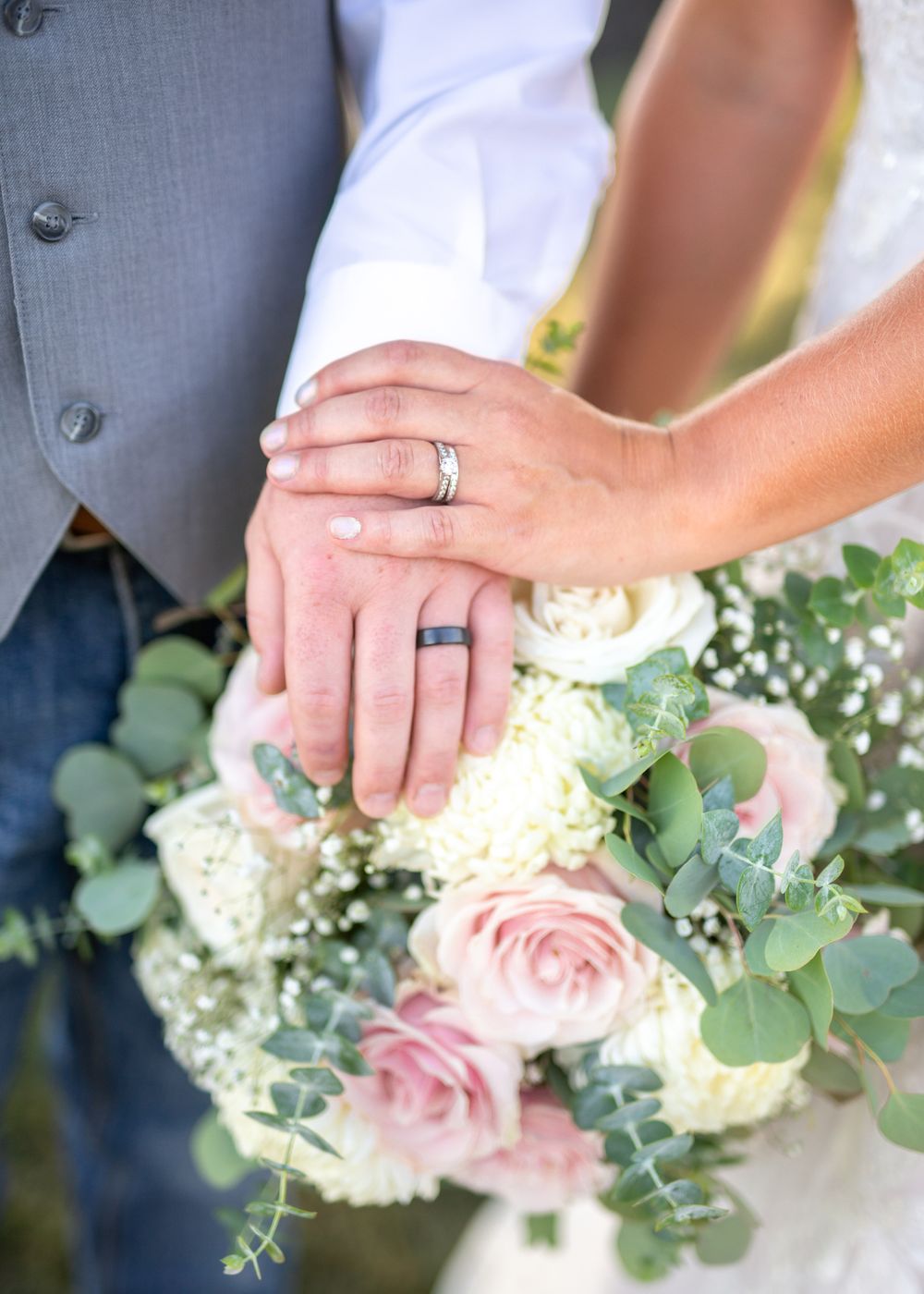 Wedding rings displayed with bouquet of pink roses and eucalyptus.