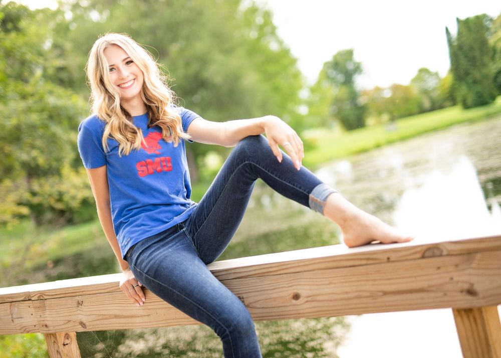 Casual outdoor photoshoot on a wooden deck with blue shirt and jeans in natural lighting.