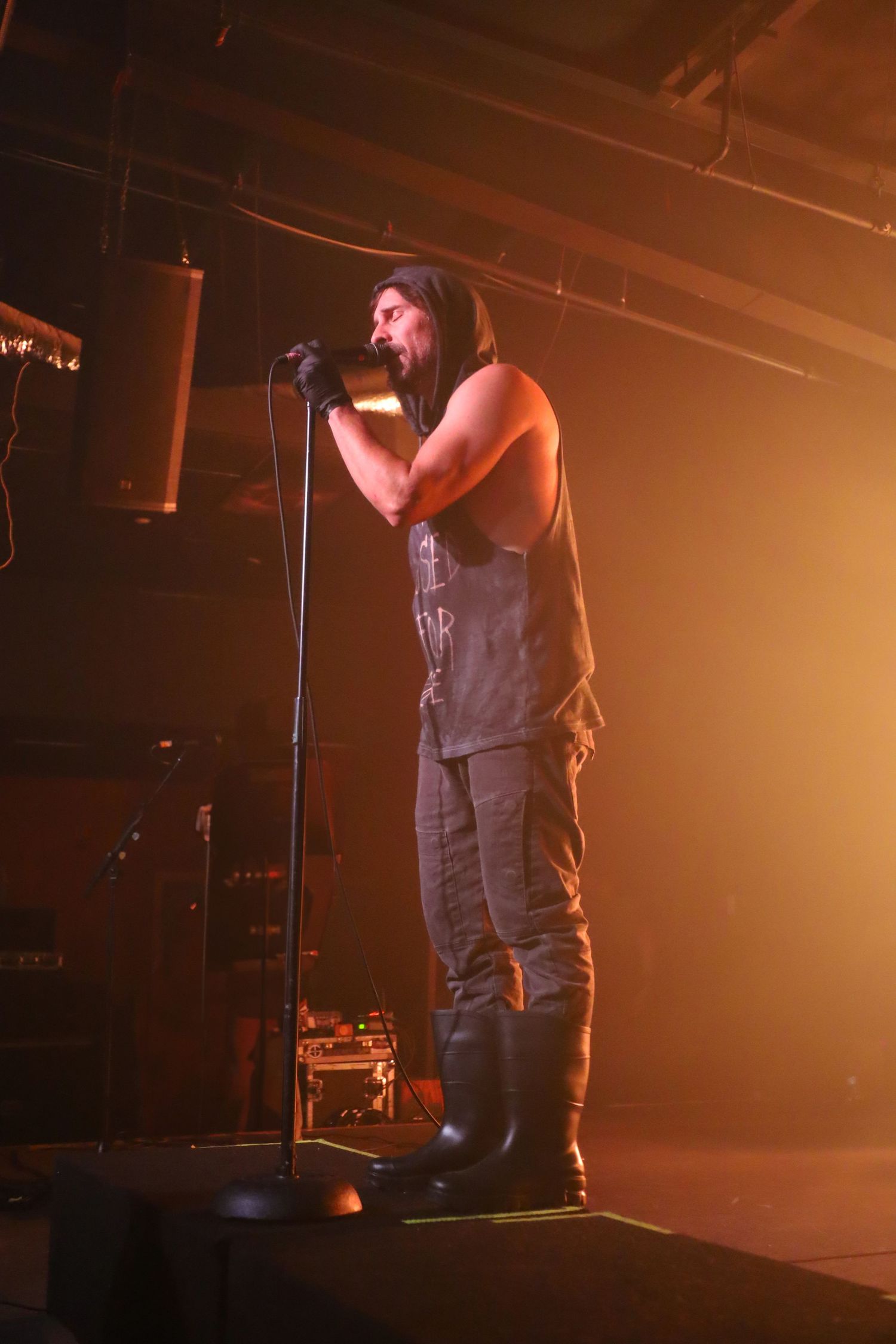 A performer stands on stage singing into a microphone under warm orange lighting during a concert performance.