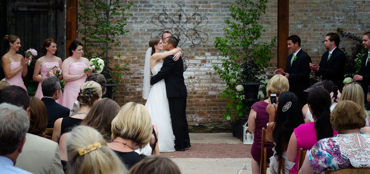 A Denver couple embracing for their first kiss at their wedding with  wedding party cheering.