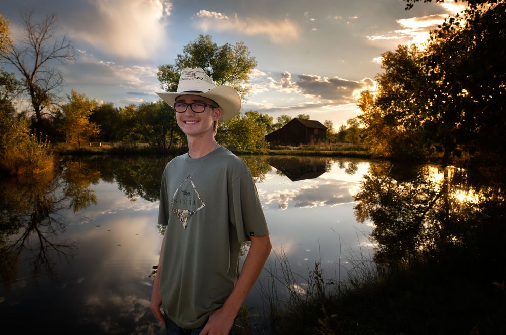 A Thornton Senior stands against a dramatic sunset sky reflected in calm lake waters.