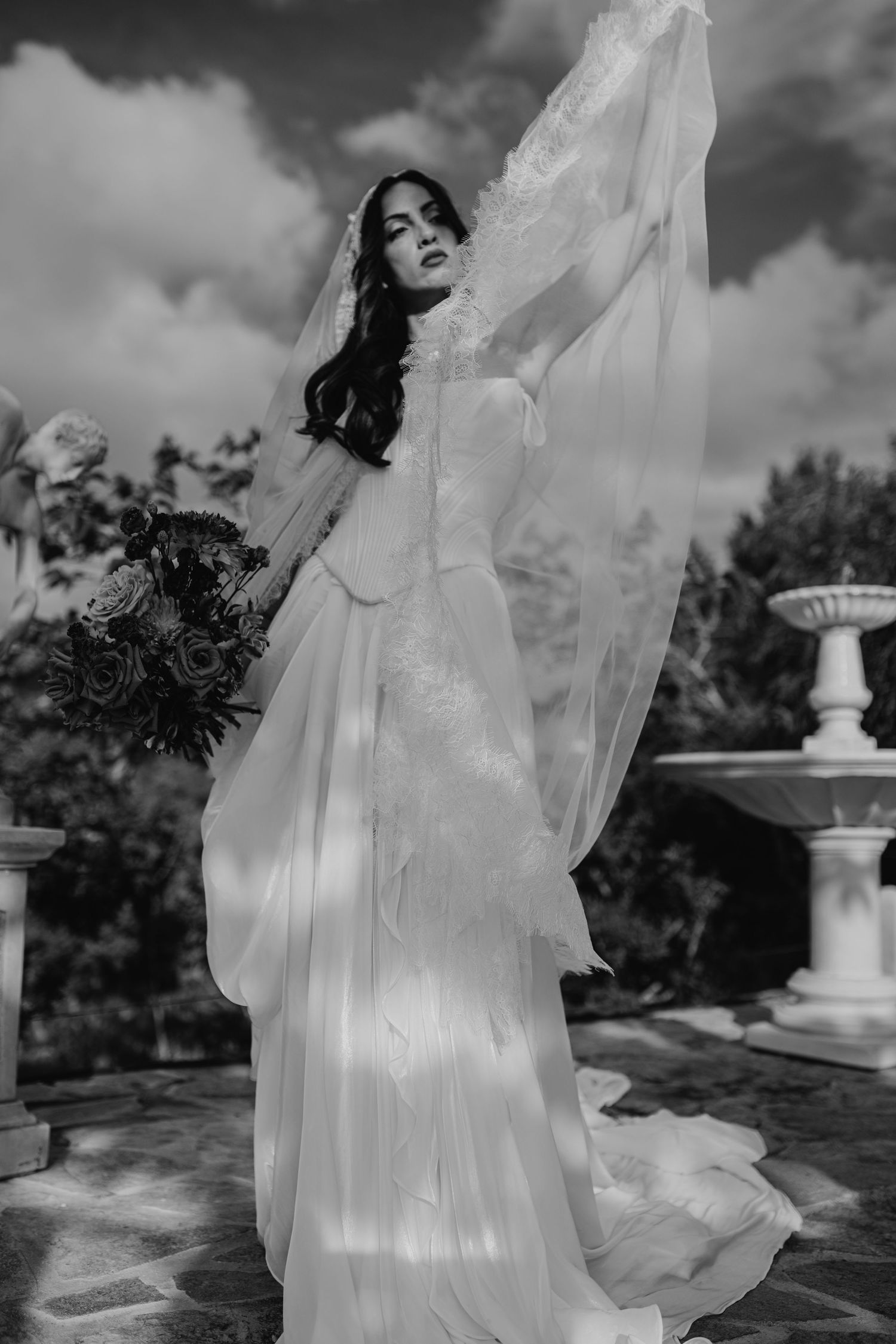 A black and white bridal portrait series showing a flowing white wedding dress and veil against a dramatic cloudy sky.