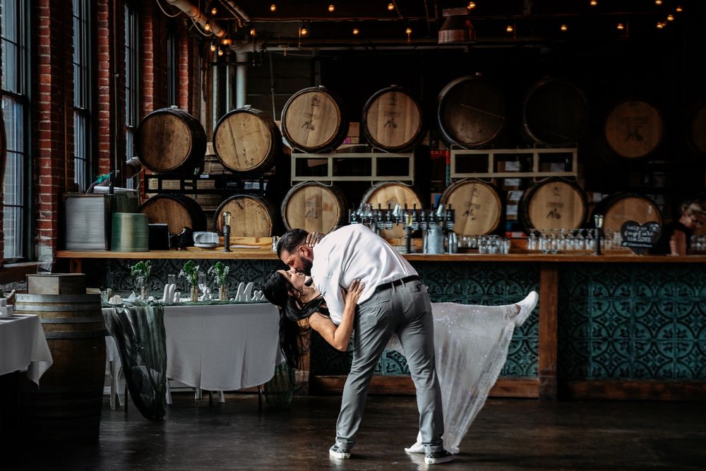 A romantic dance dip pose in front of rustic wine barrels at an elegant winery venue.