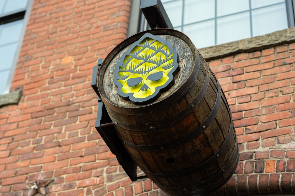 Wooden whiskey barrels with yellow logos stacked against a red brick wall.
