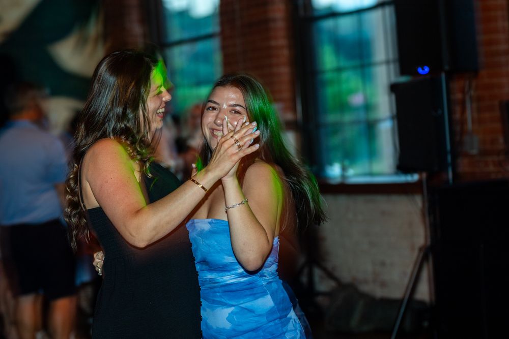Two people in blue and green attire embrace and dance together in a dimly lit setting.
