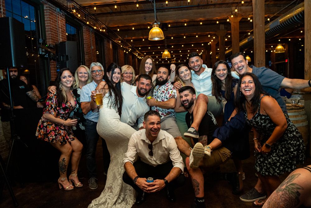 Wedding reception guests dance and celebrate on a rustic barn dance floor illuminated by string lights overhead.