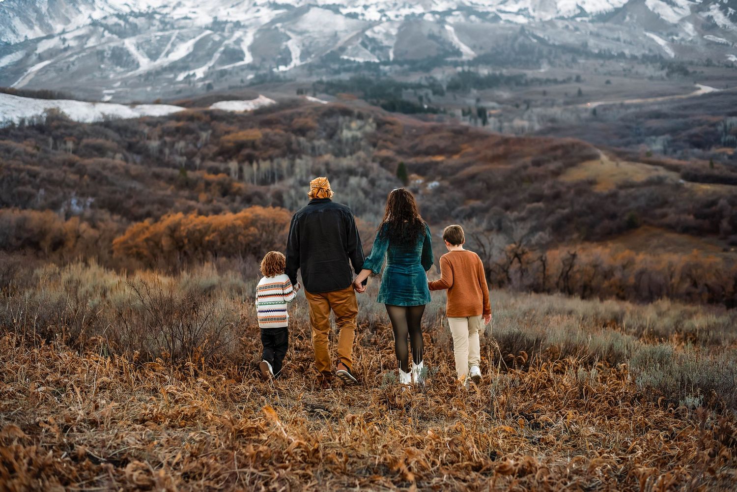 family walking towards mountains, hand in hand at snowbasin, utah.