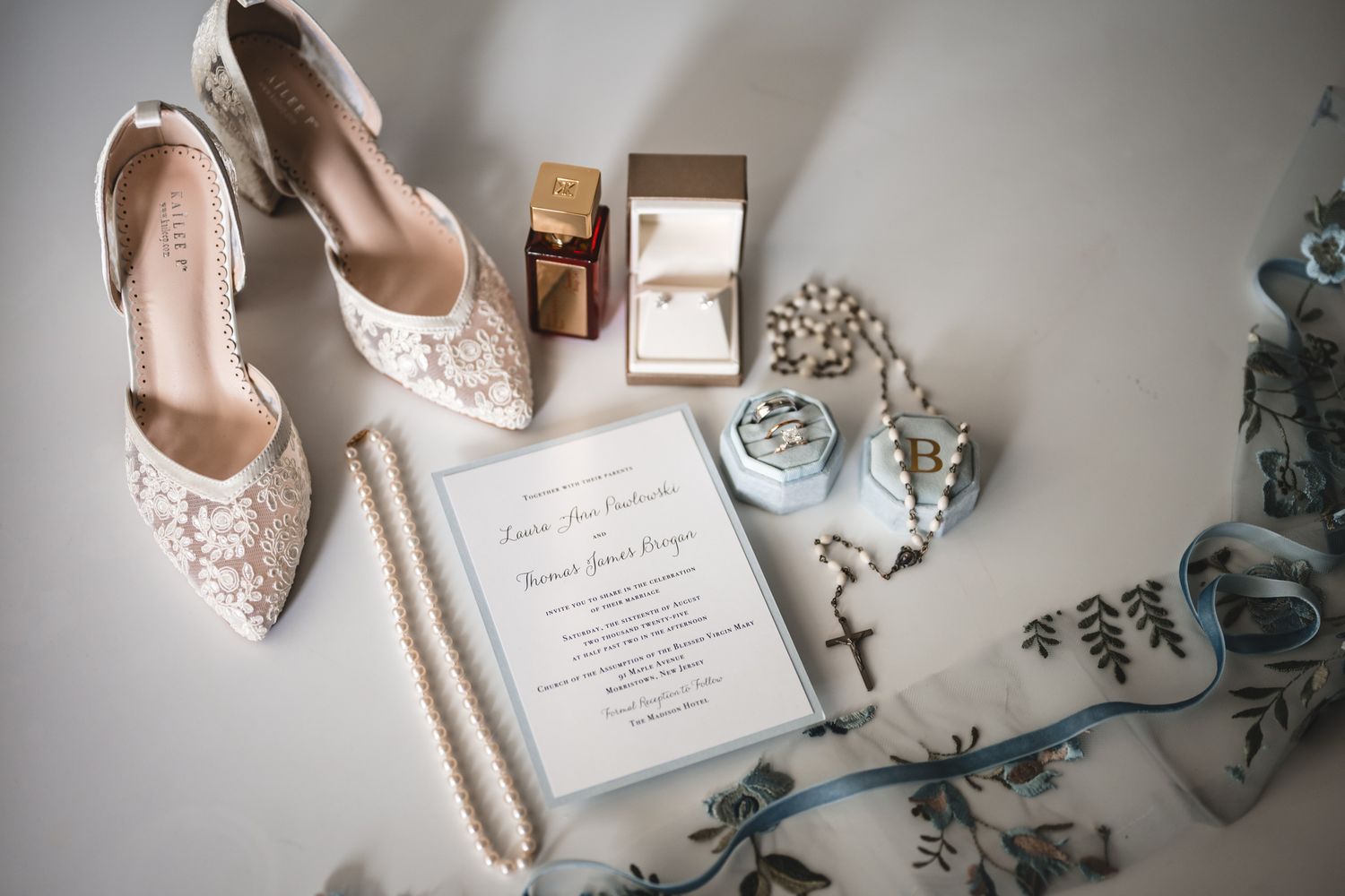 Wedding details including lace shoes, invitation, and accessories arranged on a white surface.