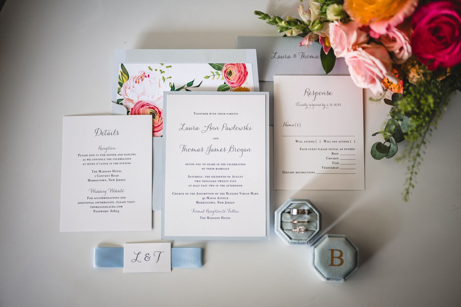 Floral wedding invitation suite with pink roses and greenery styled on white surface.