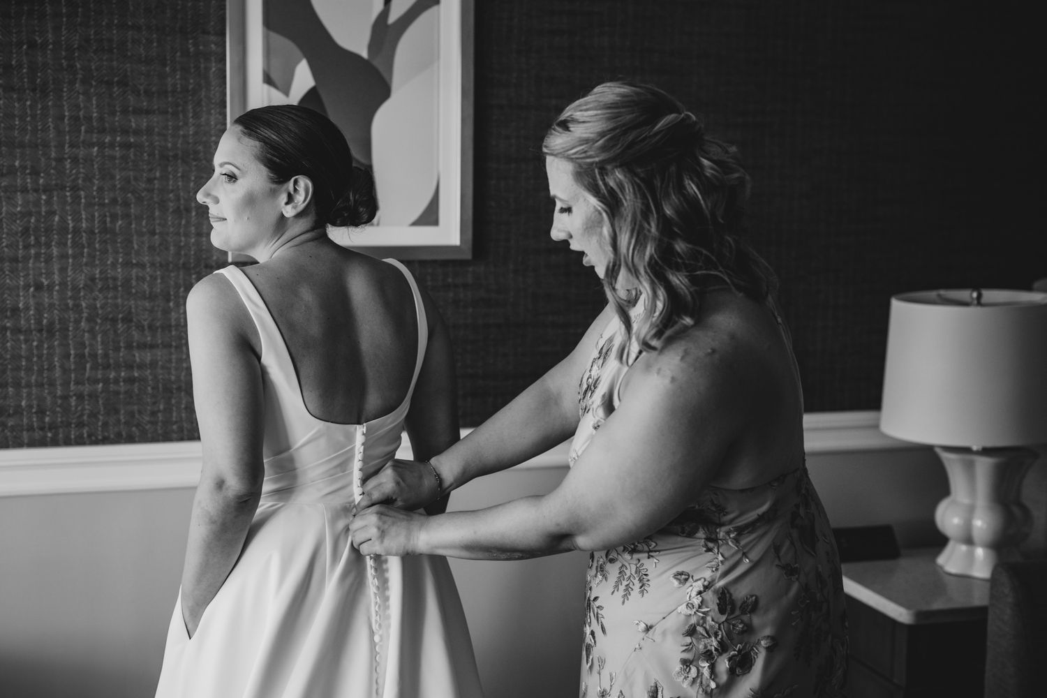 A tender moment during wedding dress preparations with modern abstract art in background.