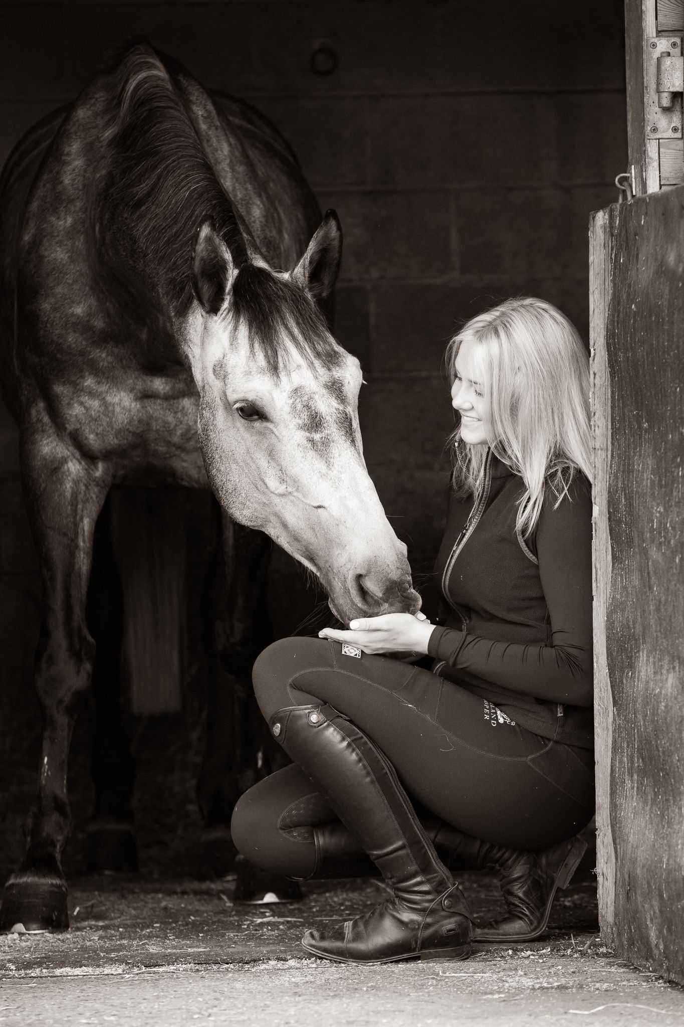 A sequence of black and white photos shows a horse nuzzling and interacting with a person in riding gear in a stable.