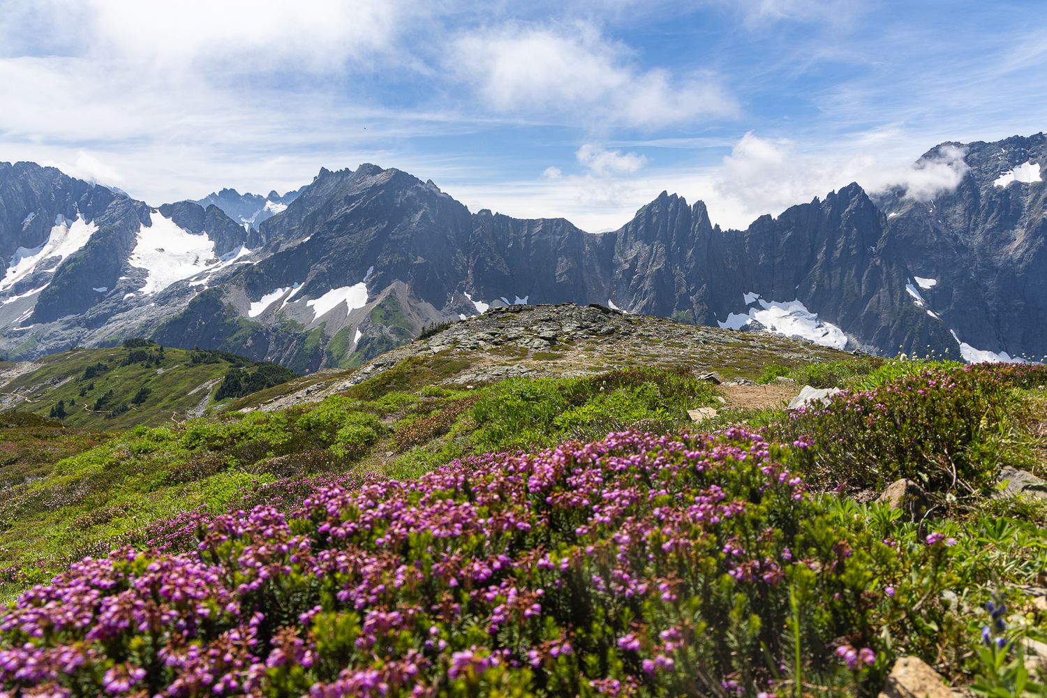 Mountain range and partly cloudy skies in the background with rocky slope leading down to a lake below.