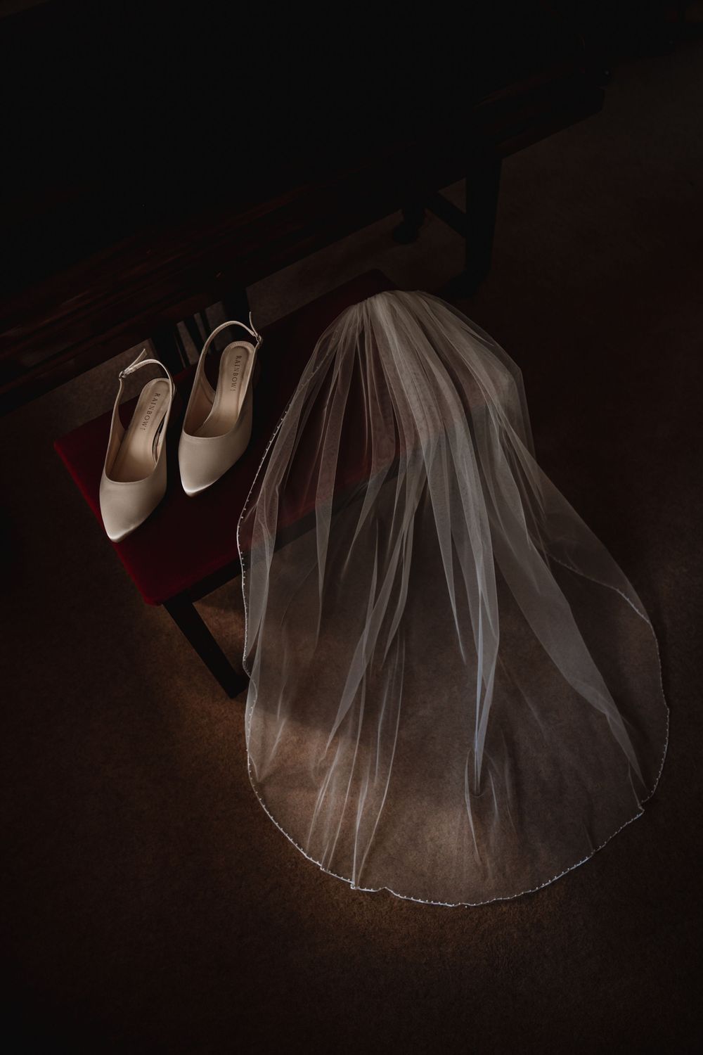 Bridal veil and white heels arranged on chair in dramatic moody lighting for wedding detail shot.