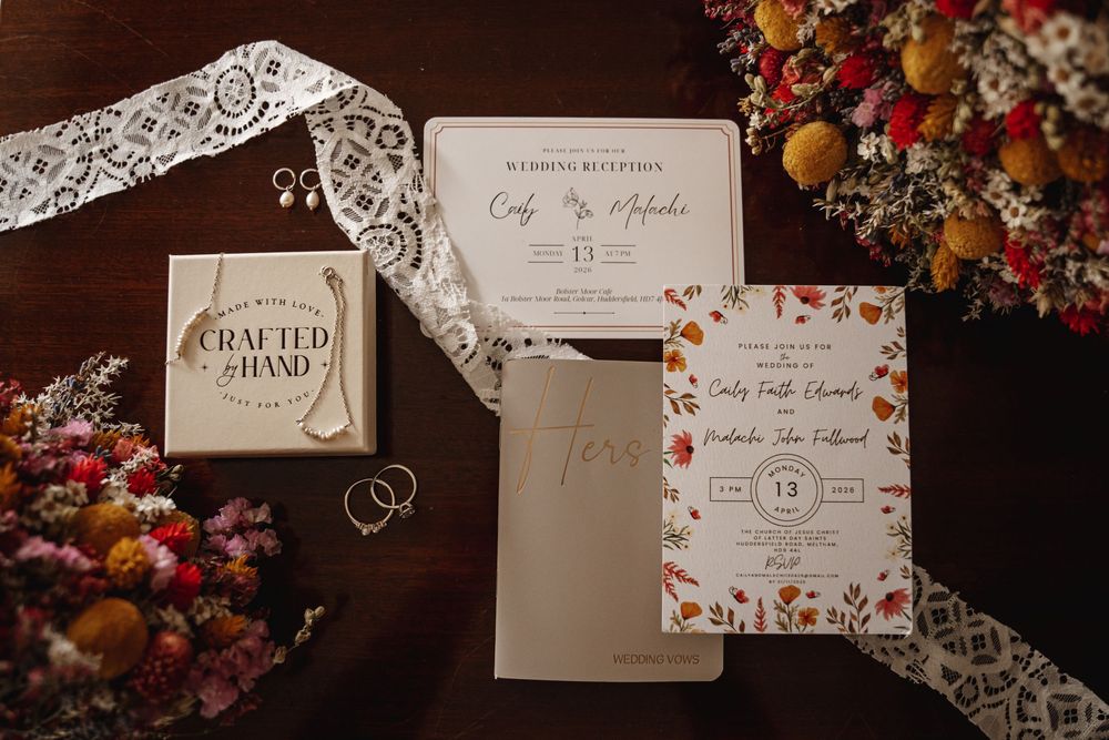 Elegant wedding invitation suite with floral accents, lace ribbon, earrings, and dried flowers on a wooden table.