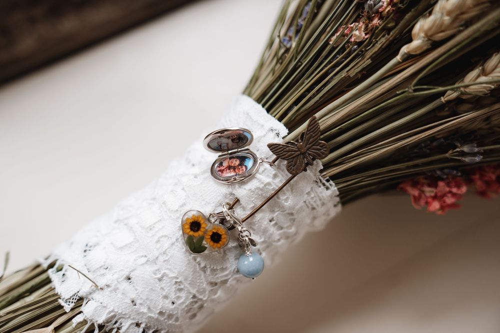 Close-up of a bridal bouquet handle adorned with lace, floral charms, and a delicate dragonfly brooch.